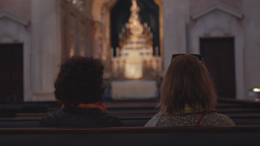Women sitting on pew inside historic church facing illuminated altar in peaceful atmosphere with soft lighting