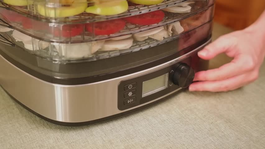 Woman adjusting settings on a food dehydrator filled with various sliced fruits and vegetables