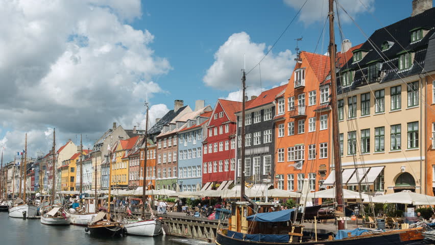 Timelapse of the historic Nyhavn waterfront, a 17th-century canal and entertainment district lined by brightly coloured townhouses, on a sunny day in Copenhagen, Denmark, zooming in.