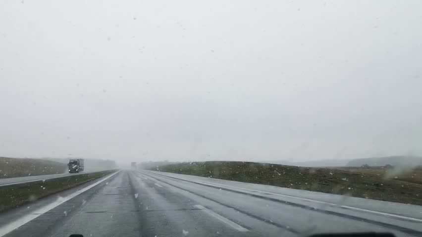 Bad driving conditions on a highway in wet snow and rainy weather. Blurry car front view. Overcast. Traffic. Slippy road. Difficult visibility. The windscreen wiper. Moving automobiles. Speed way.