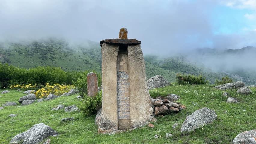 Ancient old Ossetian burial burials, vertical stone monument. Slab with ornaments on a mountain slope in a cloudy haze in North Osetia, Russia