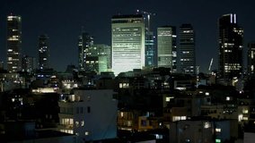 A modern city night view of some high rises and lower buildings against dark skies. one large building illuminated heavily in the middle. Tel Aviv cityscape, Israel. - Powered by Shutterstock - Get 15% off with code: PIKWIZARD15