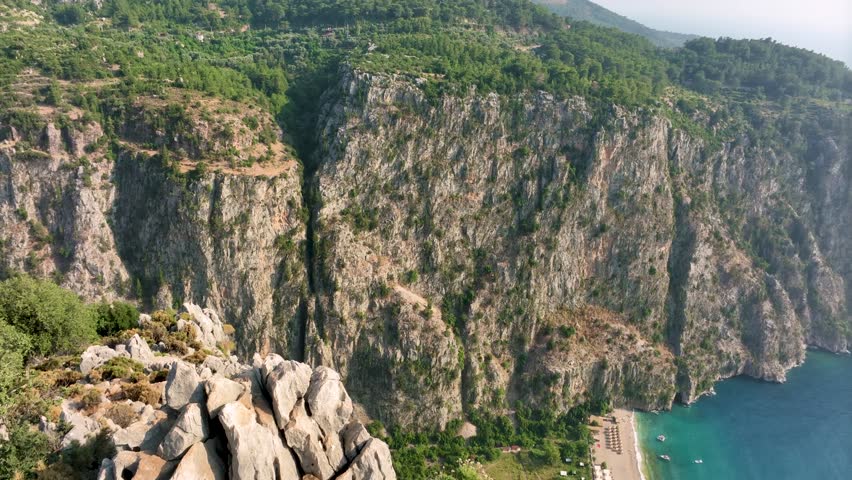Butterfly valley in fethiye, turkey, reveals a breathtaking panorama of a rocky cliff overlooking a vibrant campground nestled beside the turquoise waters of the aegean sea