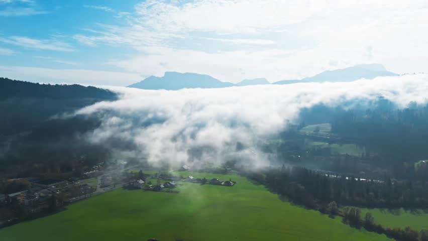 Lush landscape with mist rolling over fields beneath mountains in the French Alps