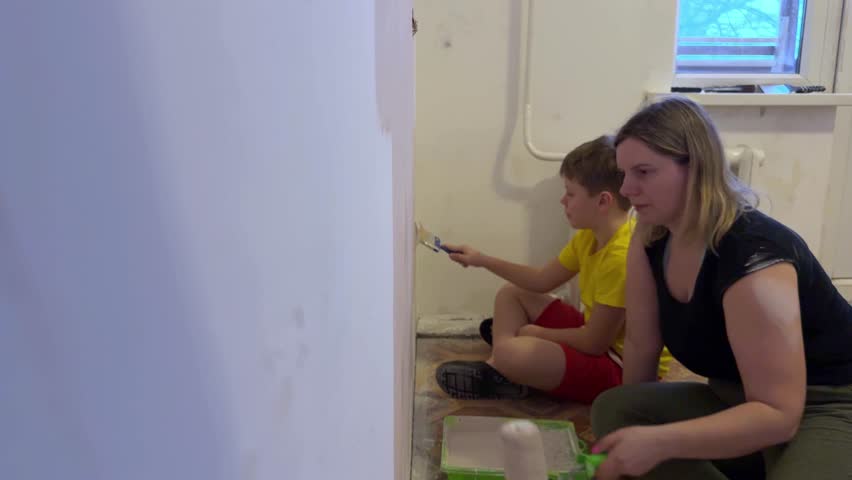 The mother and her little boy are busy painting their room, using a brush and roller for the walls. A friendly family, the new children