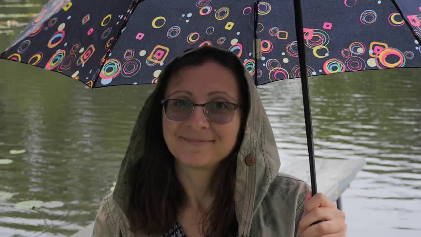 Smiling Woman with Colorful Umbrella on a Rainy Day and Lake Background