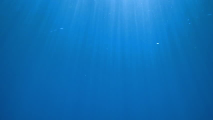 Dark blue ocean surface seen from underwater. Abstract waves underwater and rays of sunlight shining through, Sun light rays undersea deep, Underwater background with sea bottom, Mediterranean sea.