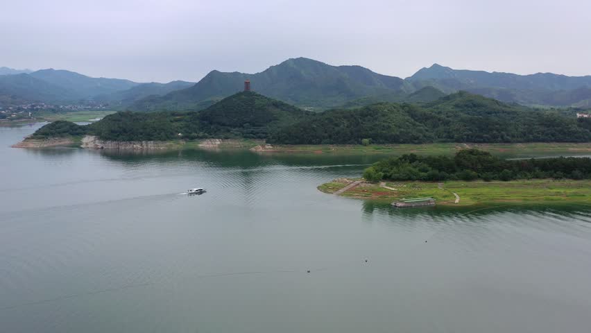 Explore jinhai lake in beijing china by air during daytime, showing mountains, lush green trees, water, and a boat cruising on the lake