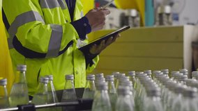 A male factory worker writing on digital tablet inspecting quality of juice bottle on conveyor belt at drink industry. Inspector working represents for responsibility and safety - Powered by Shutterstock - Get 15% off with code: PIKWIZARD15