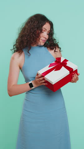 Positive smiling young woman presenting birthday green gift box stretches out hands, offer wrapped present career bonus, celebrating party sale. Girl isolated alone on blue studio background. Vertical