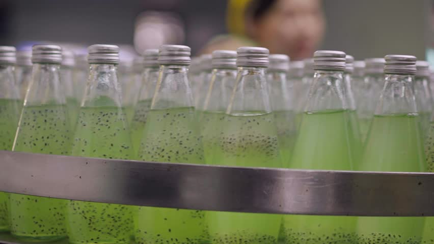 Juice bottling line for processing to production machinery on conveyor belt at drink factory. Background of worker inspecting a quality inside the bottle