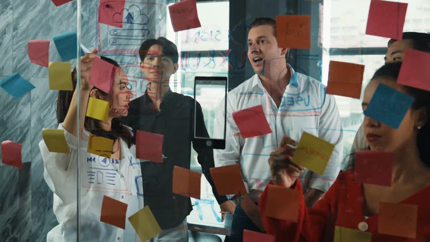 Happy professional business team brainstorming marketing idea by using colorful sticky notes to share creative idea at glass wall. Group of diverse business team discuss about strategy. Manipulator.