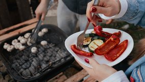 Slow motion sequence capturing woman picking grilled zucchini and red peppers with fork while man cooking mushrooms over barbecue grill outdoors. Perfect for stock about wellness or summer eating - Powered by Shutterstock - Get 15% off with code: PIKWIZARD15
