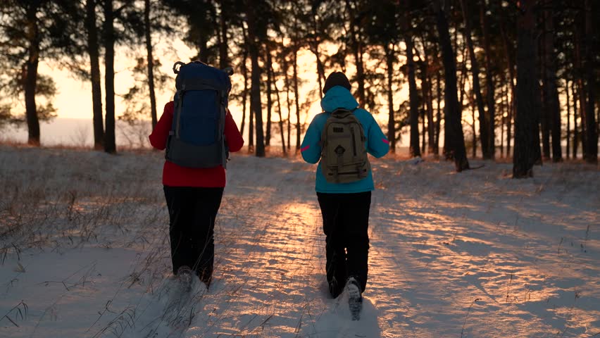 Active people vacation, healthy lifestyle, achievement. Winter expedition teamwork. Hike of successful tourist heading for success adventure. Tourist with backpack walks through snowy forest, sunset