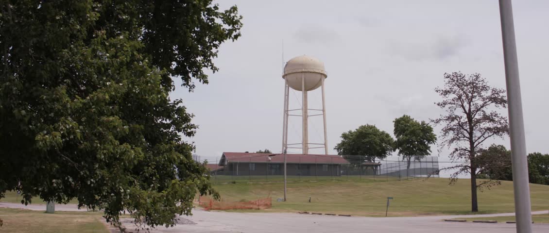 A large water tower overlooks a juvenile detention center surrounded by trees