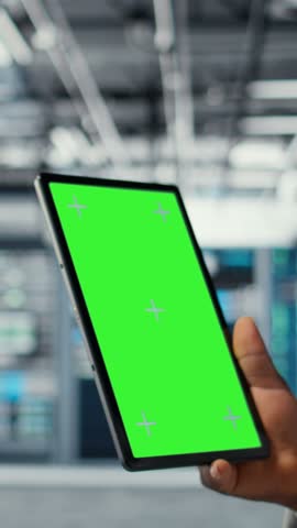 Vertical video Data center IT expert uses mockup tablet, reviewing performance dashboards of equipment rigs. Server room manager overseeing systems, examining infrastructure on chroma key device