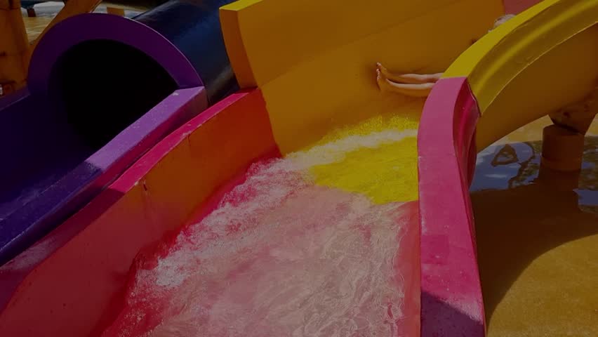 Litlle girl in bright blue swimming goggles slides down at a water park. The atmosphere of children