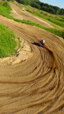 FPV drone chases motocross rider on dirt track through green countryside and forest, capturing fast turns, speed, and outdoor adventure in summer sunlight.