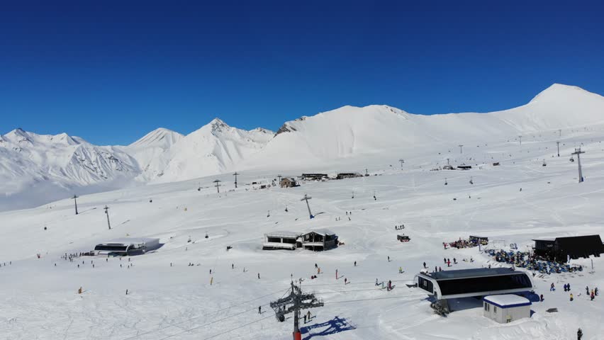 Aerial view of Gudauri ski resort in Georgia on sunny winter day. Snow-covered slopes, ski lifts, tourists, and mountain landscape.Winter sports, tourism, vacation destination, alpine adventure travel