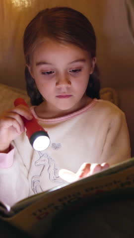 Girl, kid and reading book with flashlight at night for fairy tale or bedtime story at home. Child, relax and late evening with light or torch for novel, imagination or literature in bedroom at house