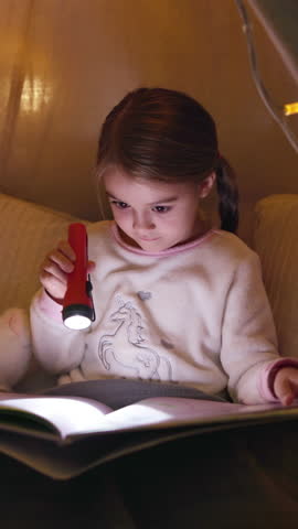 Girl, child and reading book with flashlight at night for fairy tale or bedtime story at home. Kid, relax and late evening with light or torch for novel, imagination or literature in bedroom at house