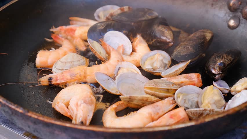 Close-up of sizzling seafood in a pan including oysters of various types and sizes and shrimp. Frying in bubbling oil. Fresh seafood cooking in an open air Asian restaurant.