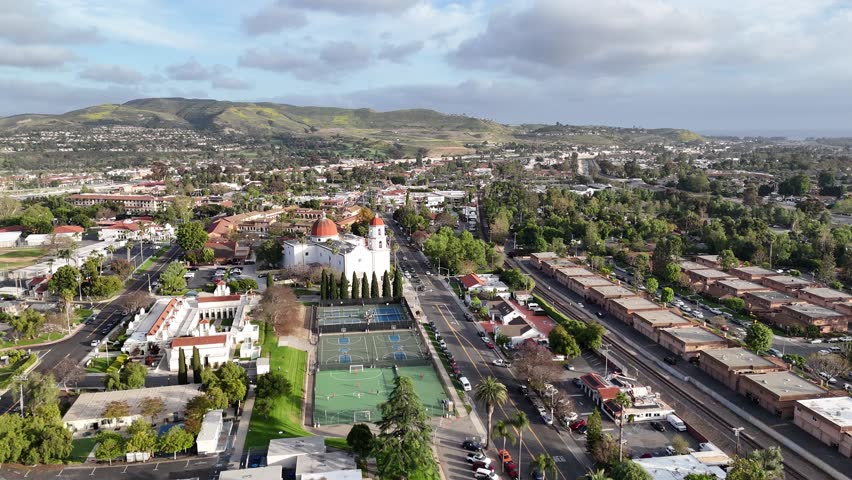 Aerial view over San Juan Capistrano, California, featuring the historic mission, library, sports courts, and an Amtrak train pulling into the downtown station.