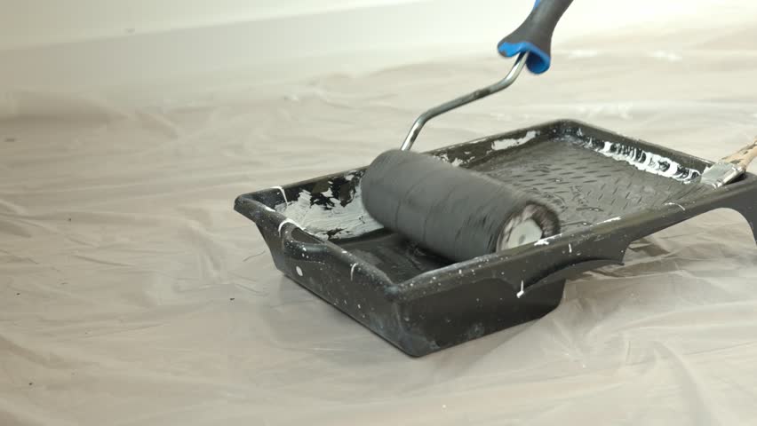 Close-up of paint roller in tray with black paint on floor covered with protective film. Concept of interior painting and DIY home renovation