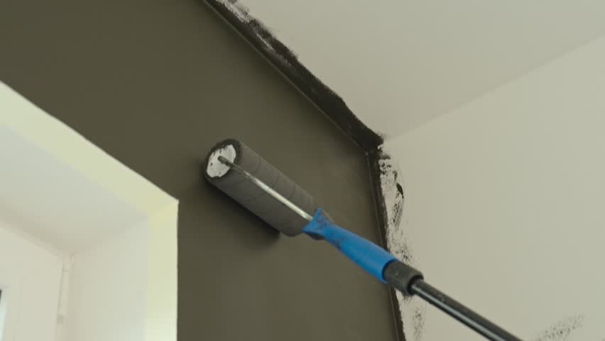 Close-up of paint roller applying dark color to wall during interior renovation. Concept of DIY painting, home improvement and redecoration in modern apartment