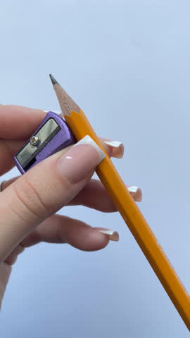Hands sharpening a pencil. Close-up video of hands with beautiful manicures sharpening a yellow pencil with a purple sharpener. Educational, back to school, stationery and creative process concept