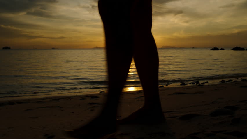 Barefoot Person Walks Slowly Along the Sandy Beach During Sunset with Dramatic Reflection on Water and Sky in Silhouette, Tranquil Dusk Stroll Concept.