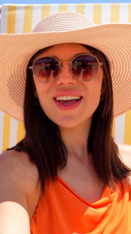 Cheerful tourist in stylish straw hat and sunglasses basking in warm sunlight, embodying carefree summer vacation mood at picturesque beach setting