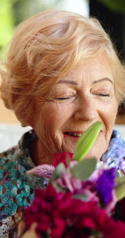 Smile, flowers and smell with old woman in home for relax, floral aroma and mothers day gift. Happiness, retirement and bouquet present with senior person in living room for celebration and plants