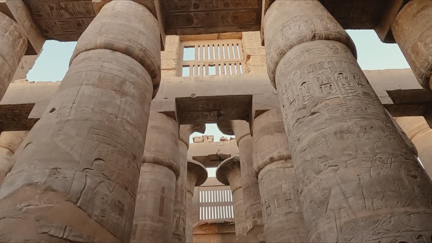 Majestic view of the towering stone columns inside the Karnak Temple complex in Luxor, Egypt. The pillars are adorned with intricate hieroglyphic carvings and symbols from ancient Egyptian history.
