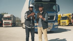 Two logistics workers analyzing route on tablet, one pointing into distance while explaining. Standing in front of parked trucks. Dressed in casual outdoor workwear under clear sky. - Powered by Shutterstock - Get 15% off with code: PIKWIZARD15