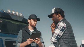 Focused male in cap holding tablet and explaining something to thoughtful his friend from same company in truck parking area. Discussing logistics or reviewing delivery route. Planning next move. - Powered by Shutterstock - Get 15% off with code: PIKWIZARD15