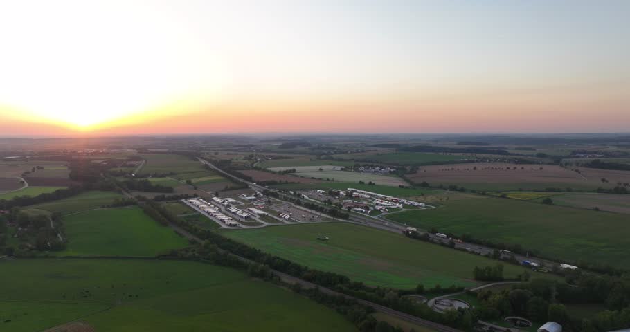 Aerial shot of a highway rest stop on the countryside surrounded by green fields during sunset