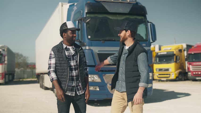 Smiling men standing shoulder to shoulder in front of blue truck posing for photo while looking directly. Celebrating teamwork or successful delivery. Sharing cheerful moment during busy logistics day