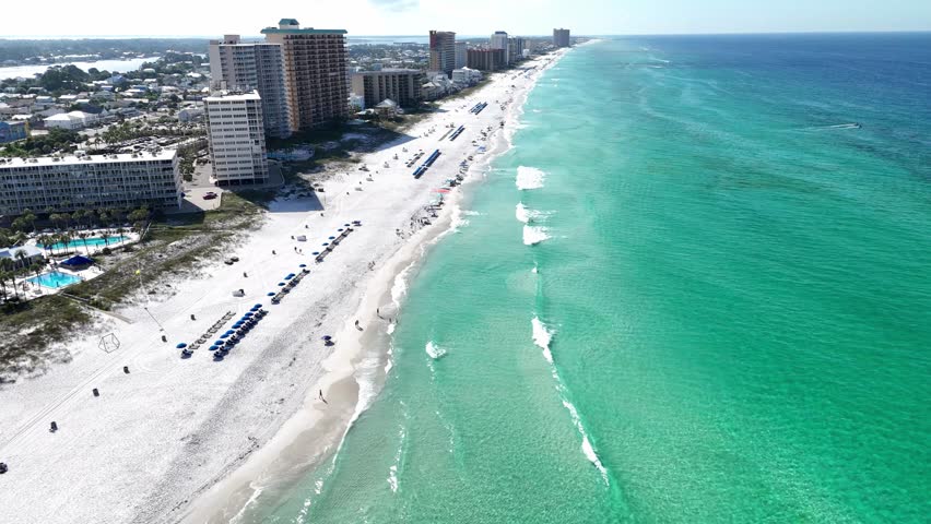 Backward aerial movement over the tropical coastline with turquoise waves and hotel buildings under sunshine, Panama City Beach, Florida, USA