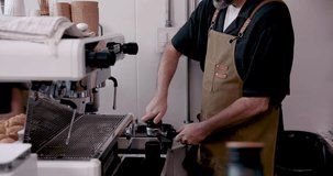 Asian senior male barista tamping ground coffee firmly into portafilter while preparing espresso shot at cafe machine station with serious expression during coffee making process - Powered by Shutterstock - Get 15% off with code: PIKWIZARD15