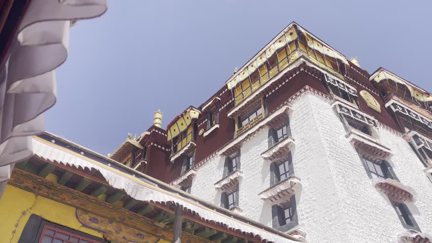 Low angle of Potala Palace reveals rich colors and ornate detailing under blue sky, slow pan right
