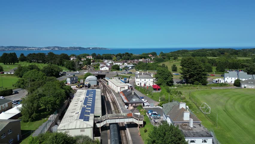 Churston, South Devon, England: DRONE VIEWS: A steam train slowly pulls into Churston railway station; the sea of Torbay is in the background. South Devon is a popular UK holiday destination.