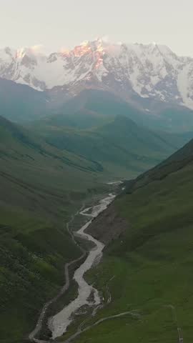 Drone aerial vertical view of Ushguli valley with winding river and majestic Shkhara Peak, highest mountain of Georgia in breathtaking beautiful Caucasus mountains range during summer.