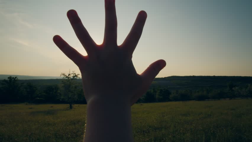 Silhouetted hand reaching up toward the bright sky with the sun shining through, symbolizing hope, freedom, and connection with nature in a peaceful moment.