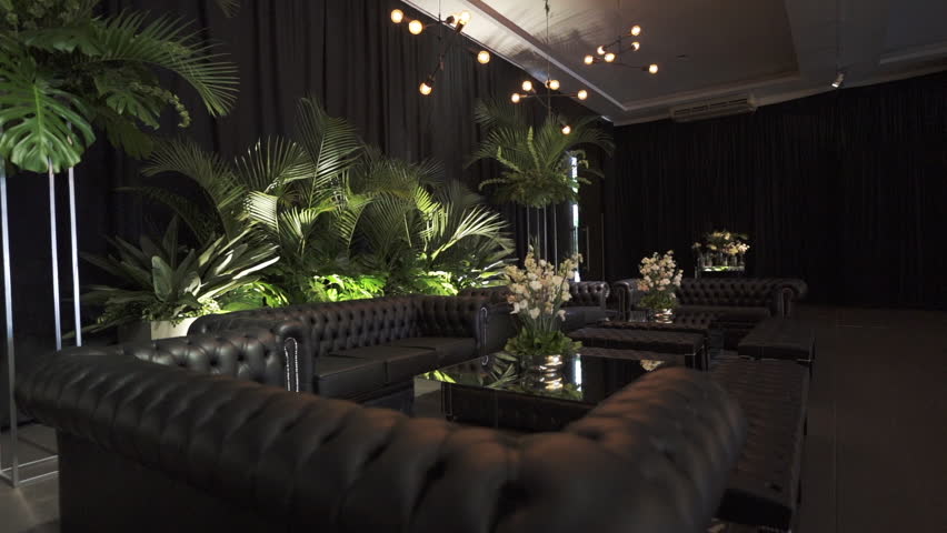 Luxury wedding lounge with black Chester sofas and tropical foliage, elegant indoor reception decor