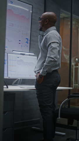 Advanced Trading Office: Excited Financial Analyst Having Phone Call, Celebrating Profitable Investments. African American Businessman Happy about Successful Financial Deal or Contract. Vertical Shot.