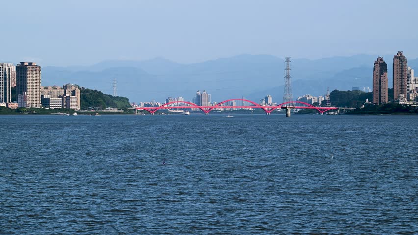 Stunning view of the pink bridge spanning the Danshui River in Taiwan at twilight, with calm waters and distant mountains. Shot on April 29, 2025.