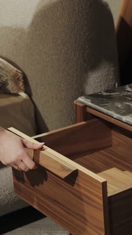 Vertical screen: A woman's hand open a drawer of a modern bedside table. Slow motion. Stylish bedside table with a beautiful marble top. wooden drawer and glass lamp. 