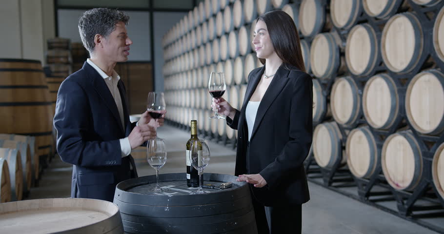 A couple enjoys a wine tasting in a winery surrounded by oak barrels