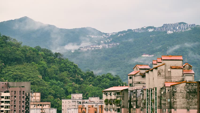 Homes nestled on the mountainside along the Northern Cross-Island Highway in Xindian, Taiwan, are enveloped in swirling mist and clouds during the afternoon, creating a serene, ethereal atmosphere.